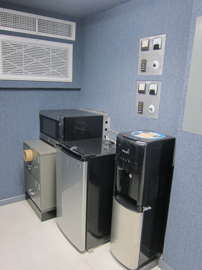A small room with a water dispenser, a refrigerator, and an oven