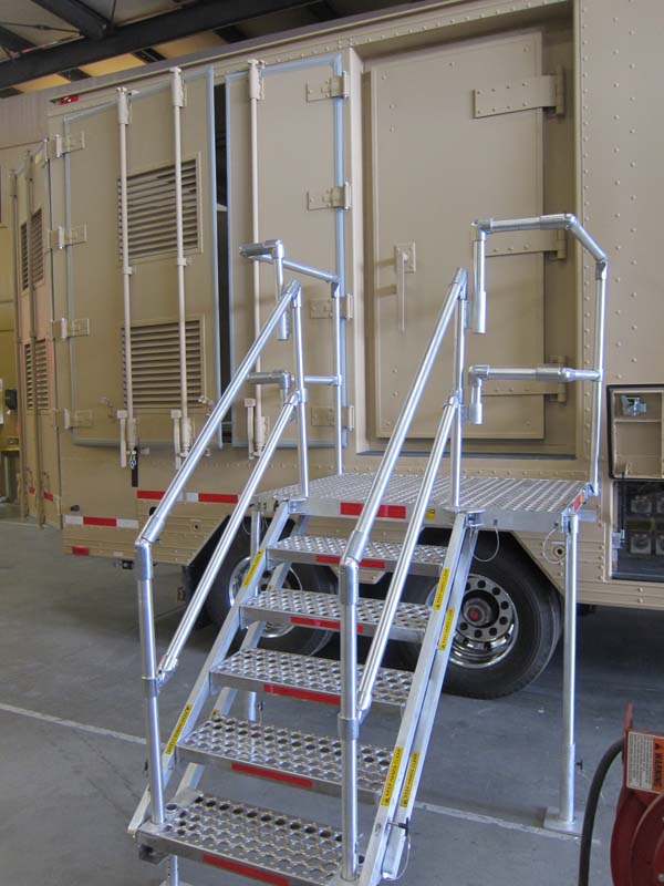 A beige mobile shelter with a 6-step metal staircase